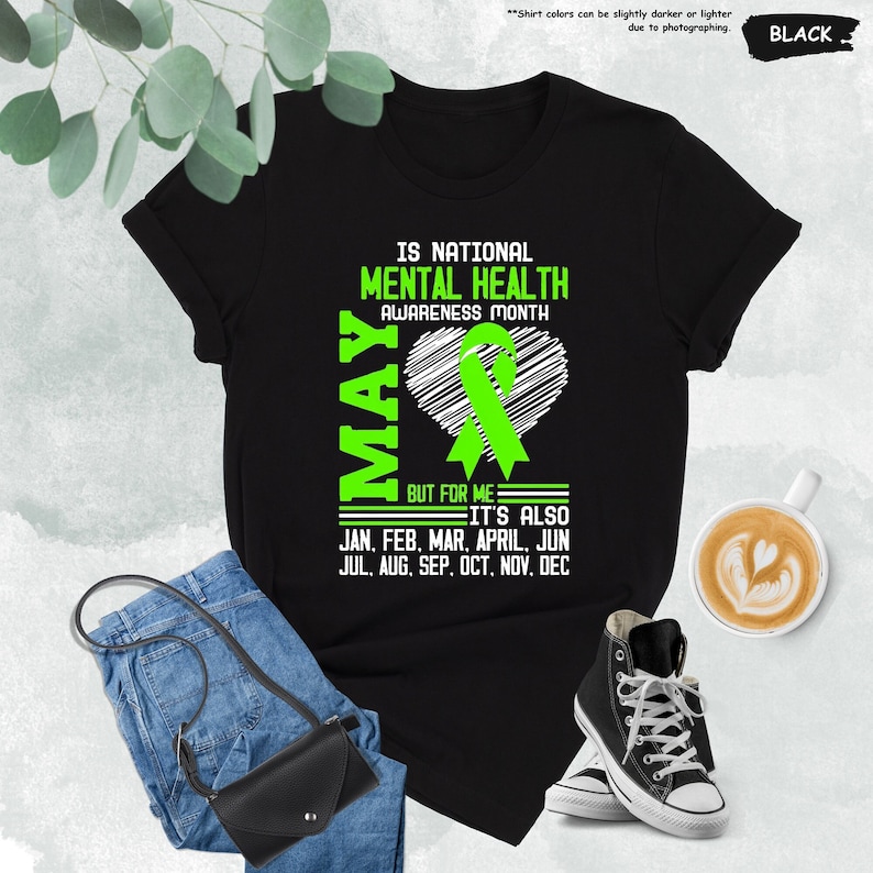 Puede incluir: Camiseta negra con texto verde que dice "Is National Mental Health Awareness Month May But for me it's also Jan, Feb, Mar, April, Jun, Jul, Aug, Sep, Oct, Nov, Dec". Una cinta verde en forma de coraz&oacute;n est&aacute; sobre el texto.