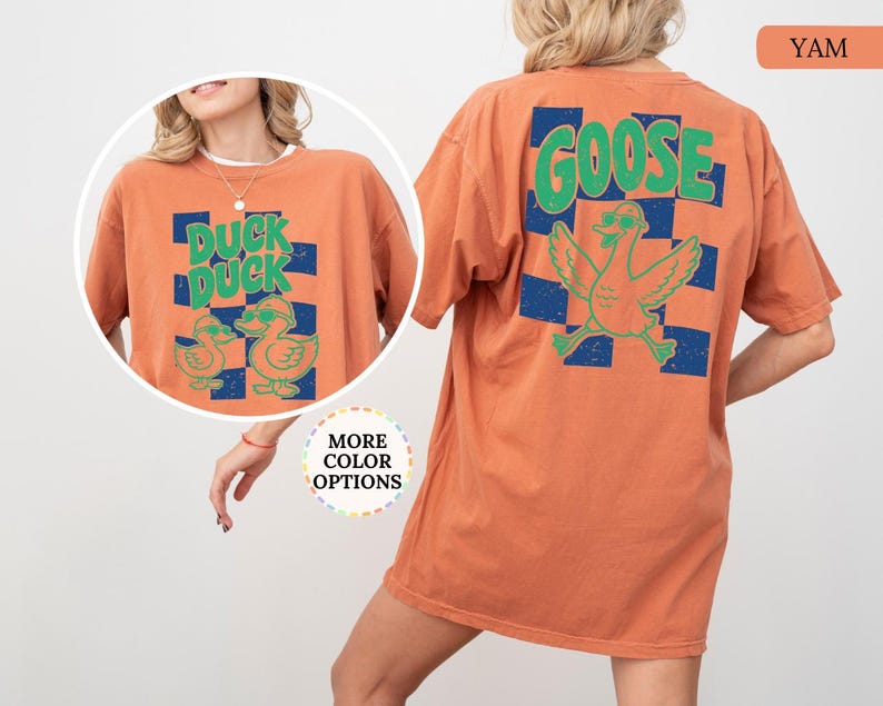 May include: An orange t-shirt featuring a graphic on the back and front. The back displays the word GOOSE in green above a green goose wearing sunglasses over a blue checkered pattern. The front shows DUCK DUCK with two ducks in sunglasses.
