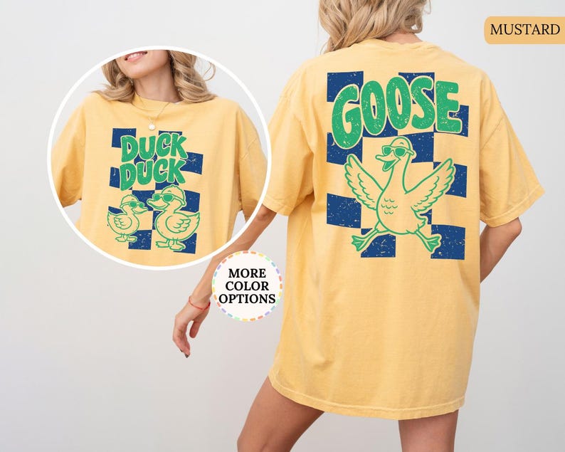 May include: A mustard yellow t-shirt featuring a dark blue checkered pattern on the back with a large green goose graphic and the text GOOSE. The front inset shows the same shirt with two ducks and the text DUCK DUCK in green.