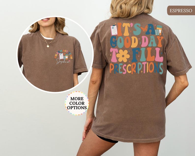 May include: Espresso-coloured t-shirt with the text "IT'S A GOOD DAY TO FILL PRESCRIPTIONS" in colourful, retro-style lettering on the back. The front features a small pharmacy-themed graphic. A woman is wearing the shirt.