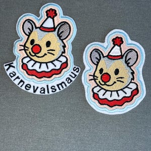 Könnte beinhalten: Zwei gestickte Aufnäher mit einer Mausfigur, die einen Clownshut und einen Rüschenkragen trägt. Die Maus hat eine rote Nase, graue Ohren und ein beiges Gesicht. Ein Aufnäher enthält den schwarzen Schriftzug "Karnevalsmaus" am unteren Rand.