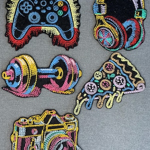 May include: A set of five embroidered patches featuring a black game controller with yellow rays, colorful headphones, a dumbbell with blue and pink weights, a slice of pizza with melting cheese, and a camera, all with vibrant neon-colored stitching.