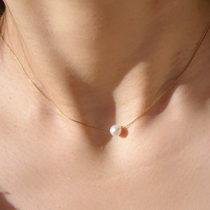 Puede incluir: Un delicado collar de cadena dorada con un solo colgante de perla blanca.