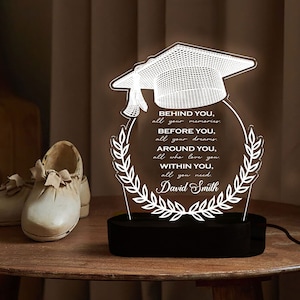 May include: A white 3D printed graduation cap with a wreath around it. The cap is illuminated and the text reads "BEHIND YOU, all your memories BEFORE YOU, all your dreams. AROUND YOU, all who love you. WITHIN YOU, all you need. David Smith".