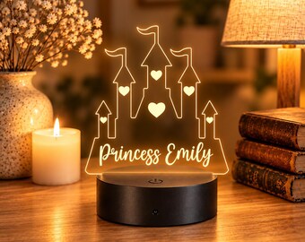 Puede incluir: Una luz nocturna de acrílico transparente con forma de castillo de cinco torres, cada una con una bandera y decorada con corazones recortados. La base es negra y cilíndrica con un botón de encendido. El texto Princess Emily está grabado.