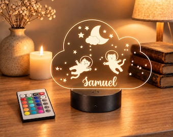 May include: A cloud-shaped LED night light featuring two cats in astronaut suits, a crescent moon, and stars. The name Samuel is engraved in script font. The light sits on a black circular base and includes a multi-colored remote control.
