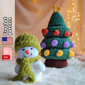 Op de afbeelding: Een gehaakte sneeuwpop met een groene hoed en sjaal naast een groene gehaakte kerstboom met kleurrijke ornamenten. De boom is bekroond met een gele ster. De afbeelding bevat de tekst "Crochet Pattern" en een PDF-pictogram.