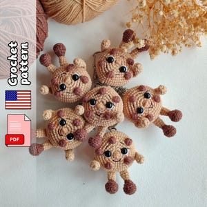 May include: Six handmade crochet giraffe keyrings in tan and brown. Each keyring features a smiling face, small arms and legs, and a keyring ring. The image also includes text that says "Crochet Pattern" and a PDF icon.