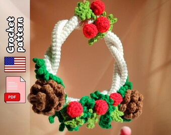 Op de afbeelding: Een handgemaakte gehaakte krans met een witte, gedraaide basis, versierd met groene bladeren, rode bessen en bruine dennenappels. De tekst "Crochet pattern" is zichtbaar, samen met een Amerikaanse vlag en een PDF-pictogram.