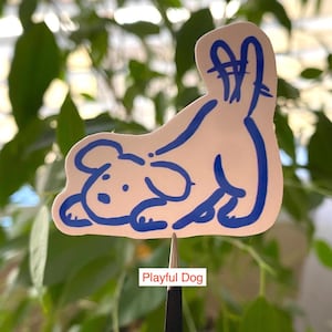以下が含まれることがあります： 尻尾を上げた遊び心のある犬の青い輪郭が描かれた白いステッカー。ステッカーの下には「Playful Dog」と書かれています。