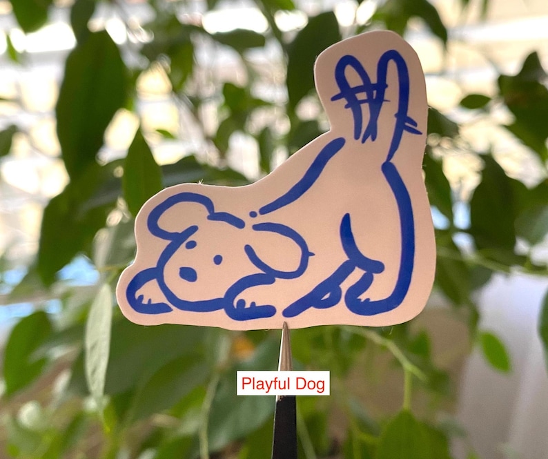 以下が含まれることがあります： 尻尾を上げた遊び心のある犬の青い輪郭が描かれた白いステッカー。ステッカーの下には「Playful Dog」と書かれています。