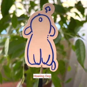 以下が含まれることがあります： 頭の上に音符がついた、吠えている犬の青い輪郭が描かれた白いステッカー。ステッカーには、画像の下に「Howling Dog」と書いてあります。