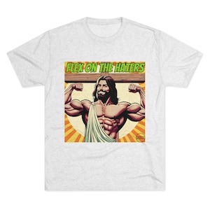 May include: A white t-shirt with a comic book style image of a muscular Jesus figure flexing his biceps. The image is set against a yellow and orange background with the text "FLEX ON THE HATERS" in green letters above the figure.
