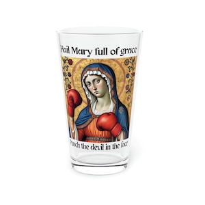 Puede incluir: Un vaso de vidrio transparente con una imagen colorida de la Virgen María usando guantes de boxeo. El texto "Hail Mary full of grace" y "punch the devil in the face" está impreso en el vaso.