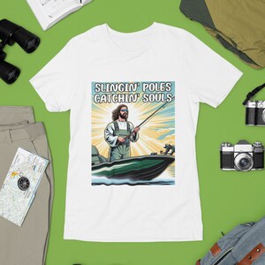 May include: White t-shirt with a graphic of Jesus fishing from a boat with the text "Slingin' Poles Catchin' Souls".