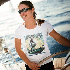 May include: White t-shirt with a graphic of a man fishing from a boat. The graphic has the text "Slingin' Poles Catchin' Souls".