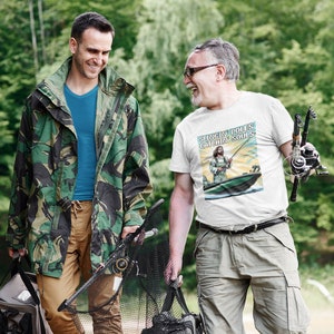 May include: Two people walking in a forest, one wearing a camouflage jacket and the other wearing a white t-shirt with the text "Slingin' Poles Catchin' Souls".