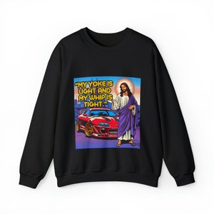 Puede incluir: Sudadera negra con un estampado gráfico de Jesús de pie junto a un coche deportivo rojo. El texto en el gráfico dice "My yoke is light and my whip is tight."