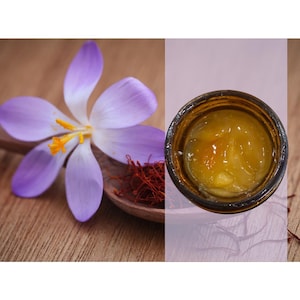 May include: A small glass jar filled with a yellow, translucent substance, possibly a honey or jam. The jar is sitting on a wooden surface next to a purple crocus flower and strands of red saffron.