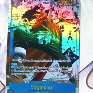Pode incluir: Um cart&atilde;o de jogo azul e vermelho com um personagem do anime One Piece. O personagem &eacute; Sogeking, um atirador de elite da ilha Sniper. O cart&atilde;o tem um n&iacute;vel de poder de 6000 e um contador de +1000. O texto do cart&atilde;o diz "...&eacute; o rei atirador de elite!" e "Tamb&eacute;m trate o nome deste cart&atilde;o como [Usopp] de acordo com as regras. Ao jogar: Retorne at&eacute; 1 personagem com um custo de 6 ou menos para a m&atilde;o do propriet&aacute;rio. Em seguida, compre 2 cartas e descarte 2 cartas de sua m&atilde;o."