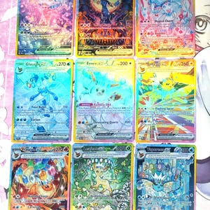 May include: Nine Pokemon trading cards featuring various Pokemon characters, including Espeon, Umbreon, Sylveon, Glaceon, Eevee, Jolteon, Flareon, Leafeon, and Vaporeon. The cards are holographic and feature colorful backgrounds and illustrations.
