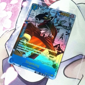 Pode incluir: Um cart&atilde;o de negocia&ccedil;&atilde;o hologr&aacute;fico com um personagem do anime One Piece. O cart&atilde;o &eacute; azul e apresenta um personagem chamado Sogeking, que &eacute; um atirador de elite. O cart&atilde;o tem um n&iacute;vel de poder de 6000 e um valor de contador de +1000. O texto do cart&atilde;o diz: "Tamb&eacute;m trate o nome deste cart&atilde;o como [Usopp] de acordo com as regras. Ao jogar, devolva at&eacute; 1 personagem com um custo de 6 ou menos para a m&atilde;o do propriet&aacute;rio. Em seguida, compre 2 cartas e descarte 2 cartas de sua m&atilde;o."