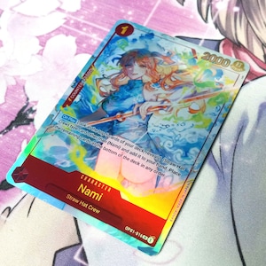 Puede incluir: Una carta de juego de comercio hologr&aacute;fica con Nami del equipo de Sombrero de Paja en la serie de anime One Piece. La carta tiene un fondo azul y naranja con un efecto hologr&aacute;fico. La carta tiene un nivel de poder de 2000 y un valor de contador de 1000. El texto en la carta dice "Al jugar, mira las 5 cartas superiores de tu mazo, revela 1 carta de tipo (Equipo de Sombrero de Paja) que no sea (Nami) y a&ntilde;&aacute;dela a tu mano. Coloca las cartas restantes en la parte inferior del mazo en cualquier orden."