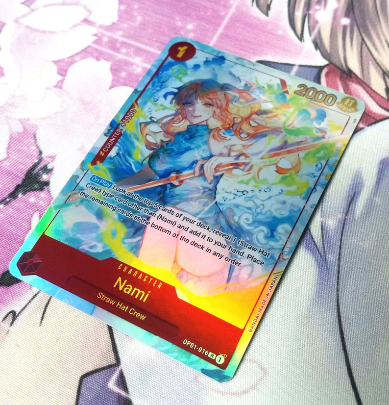 Puede incluir: Una carta de juego de comercio hologr&aacute;fica con Nami del equipo de Sombrero de Paja en la serie de anime One Piece. La carta tiene un fondo azul y naranja con un efecto hologr&aacute;fico. La carta tiene un nivel de poder de 2000 y un valor de contador de 1000. El texto en la carta dice "Al jugar, mira las 5 cartas superiores de tu mazo, revela 1 carta de tipo (Equipo de Sombrero de Paja) que no sea (Nami) y a&ntilde;&aacute;dela a tu mano. Coloca las cartas restantes en la parte inferior del mazo en cualquier orden."