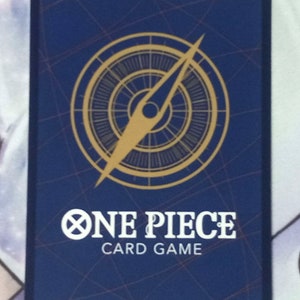 Puede incluir: Una tarjeta azul con un dise&ntilde;o de br&uacute;jula dorada y el texto "ONE PIECE CARD GAME".