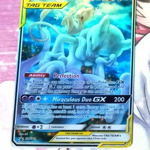 May include: A Pokémon trading card featuring Mewtwo & Mew GX. The card has a blue and white color scheme with the text "TAG TEAM" and "Miraculous Duo GX 200". The card also has the text "HP 270".
