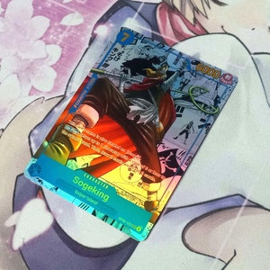 Pode incluir: Um cart&atilde;o de jogo azul e branco com um personagem chamado Sogeking do anime One Piece. O cart&atilde;o tem um n&iacute;vel de poder de 6000 e um valor de contador de +1000. O texto do cart&atilde;o diz: "Ao jogar: Escolha at&eacute; 3 personagens com um custo de 6 ou menos para a m&atilde;o do propriet&aacute;rio. Em seguida, compre 2 cartas."