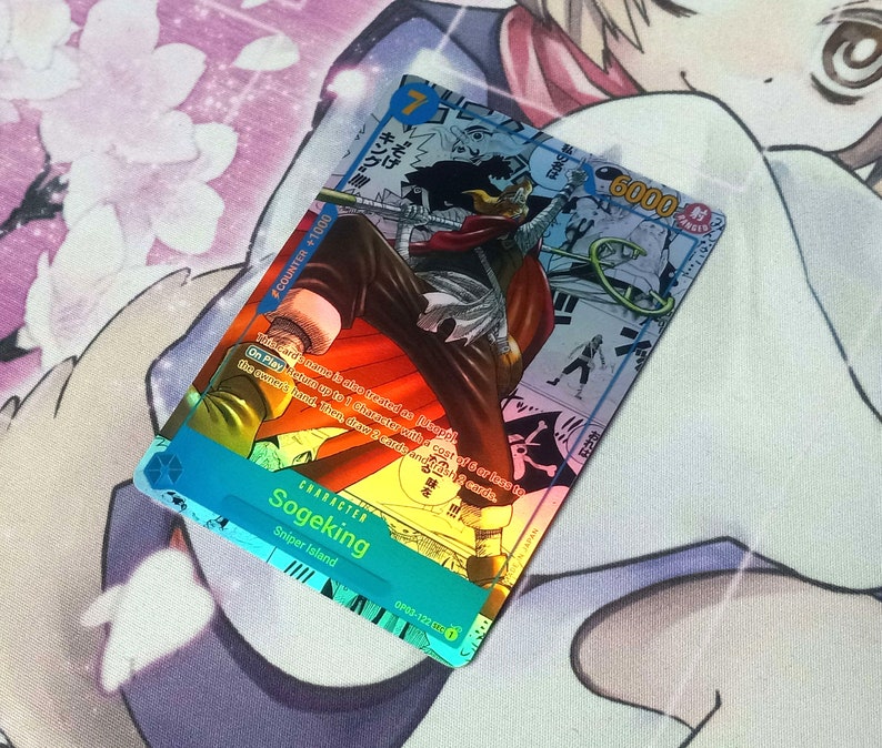 Pode incluir: Um cart&atilde;o de jogo azul e branco com um personagem chamado Sogeking do anime One Piece. O cart&atilde;o tem um n&iacute;vel de poder de 6000 e um valor de contador de +1000. O texto do cart&atilde;o diz: "Ao jogar: Escolha at&eacute; 3 personagens com um custo de 6 ou menos para a m&atilde;o do propriet&aacute;rio. Em seguida, compre 2 cartas."