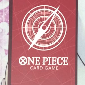 May include: A red card with a white compass and the text "ONE PIECE CARD GAME" in white.