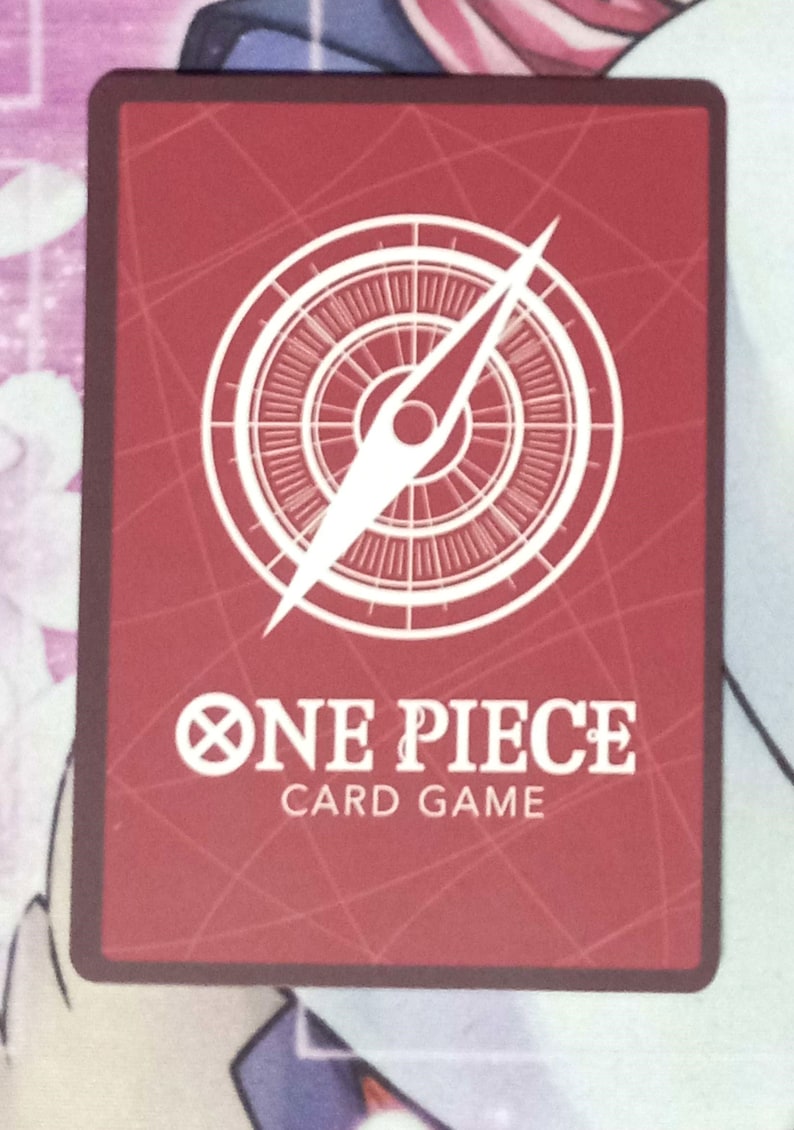May include: A red card with a white compass and the text "ONE PIECE CARD GAME" in white.