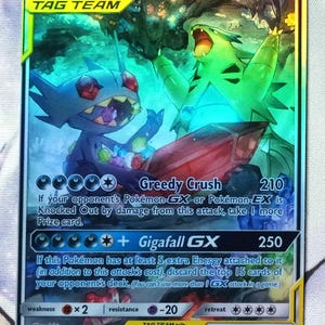 May include: A Pokemon trading card featuring Mega Sableye & Tyranitar GX. The card is holographic and features the Pokemon in a dynamic pose. The card has a HP of 280 and has two attacks: Greedy Crush and Gigafall GX.