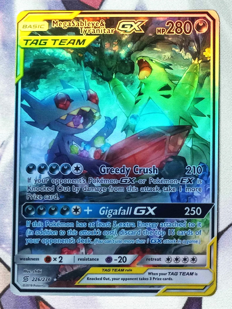 May include: A Pokemon trading card featuring Mega Sableye & Tyranitar GX. The card is holographic and features the Pokemon in a dynamic pose. The card has a HP of 280 and has two attacks: Greedy Crush and Gigafall GX.