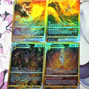 May include: Four Pokemon trading cards featuring the VSTAR versions of Palkia, Dialga, Giratina, and Arceus. The cards are gold and have holographic foil accents. Each card features a different Pokemon with its name and attack powers listed.