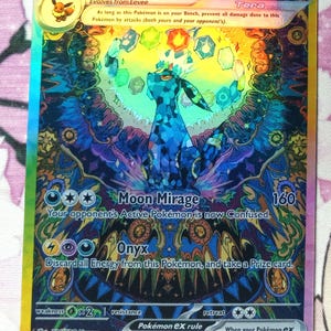 May include: A Pokemon trading card featuring Umbreon EX, a dark blue and purple Pokemon with glowing eyes. The card has a holographic finish and features the text "Moon Mirage" and "Onyx".