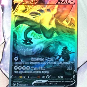 May include: A holographic Pokemon trading card featuring Lugia V, a blue and white bird Pokemon with a rainbow background. The card has a HP of 220 and features two attacks: Read the Wind and Aero Dive. The card is from the Sword & Shield - Fusion Strike set.