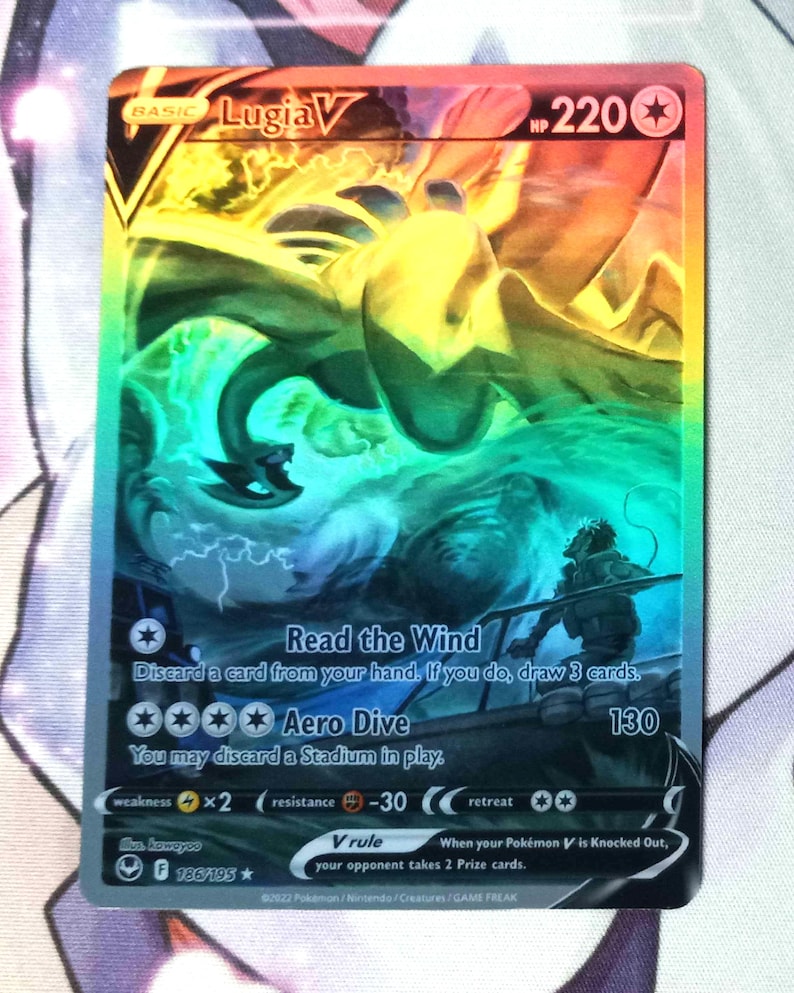 May include: A holographic Pokemon trading card featuring Lugia V, a blue and white bird Pokemon with a rainbow background. The card has a HP of 220 and features two attacks: Read the Wind and Aero Dive. The card is from the Sword & Shield - Fusion Strike set.