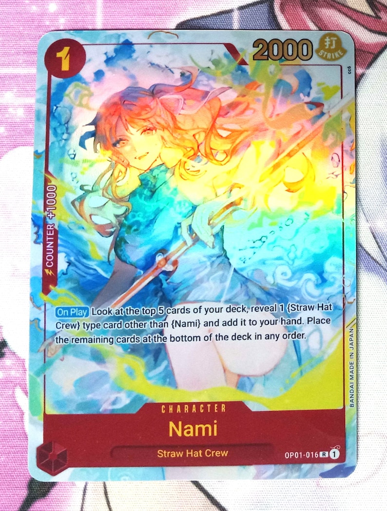 Puede incluir: Una carta de intercambio con Nami del equipo de Sombrero de Paja en el anime One Piece. La carta es azul y amarilla con un efecto hologr&aacute;fico. La carta tiene un nivel de poder de 2000 y un valor de contador de +1000. El texto de la carta dice: "Al jugar Mira las 5 cartas superiores de tu mazo, revela 1 carta de tipo (Equipo de Sombrero de Paja) que no sea (Nami) y a&ntilde;&aacute;dela a tu mano. Coloca las cartas restantes en la parte inferior del mazo en cualquier orden."