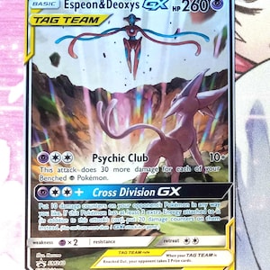 May include: A Pokémon trading card featuring Espeon & Deoxys GX. The card has a colorful background with two Pokémon characters. The card text includes "Psychic Club" and "Cross Division GX". The card is a TAG TEAM card.
