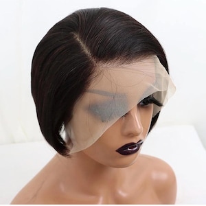 Puede incluir: Peluca corta, marrón oscuro, con encaje frontal. La peluca presenta una raya de aspecto natural y está peinada con un corte bob elegante. El encaje frontal es visible y la peluca parece estar sobre una cabeza de maniquí.