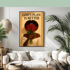 May include: A framed art print featuring a woman holding a bouquet of red roses, with the text "GOD'S PLAN IS BETTER" in black. The woman is wearing a white off-the-shoulder top. The artwork is displayed in a living room setting.