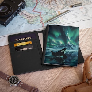 May include: Black passport holder with a design of a killer whale swimming in the ocean with the aurora borealis in the background. The holder has slots for cards and a passport.