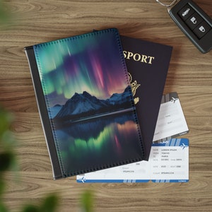 May include: A black passport cover with a vibrant image of the Northern Lights over a mountain range and a reflective lake. A dark blue passport, boarding passes, and a car key are also visible on a wooden surface.