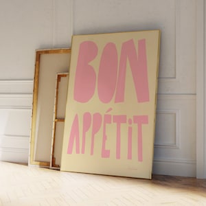 May include: A framed print with a light yellow background and pink lettering that says "Bon Appetit".