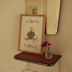 May include: A framed artwork featuring a whimsical perfume bottle design in yellow and black, with the word "PARFUM" below. The artwork is in a light wood frame, resting on a small table with a vase of pink flowers.