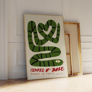 Könnte beinhalten: Eine grün-schwarz gestreifte Schlange mit einem gelben Auge ist auf einem weißen Hintergrund zu einem Herz geformt. Der Text "BEWARE OF SNAKE (CUDDLES TOO TIGHT)" ist in Rot unter der Schlange geschrieben.