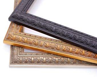 May include: Three ornate picture frames in black, gold, and silver. The frames are stacked on top of each other, with the black frame on top and the silver frame on the bottom.
